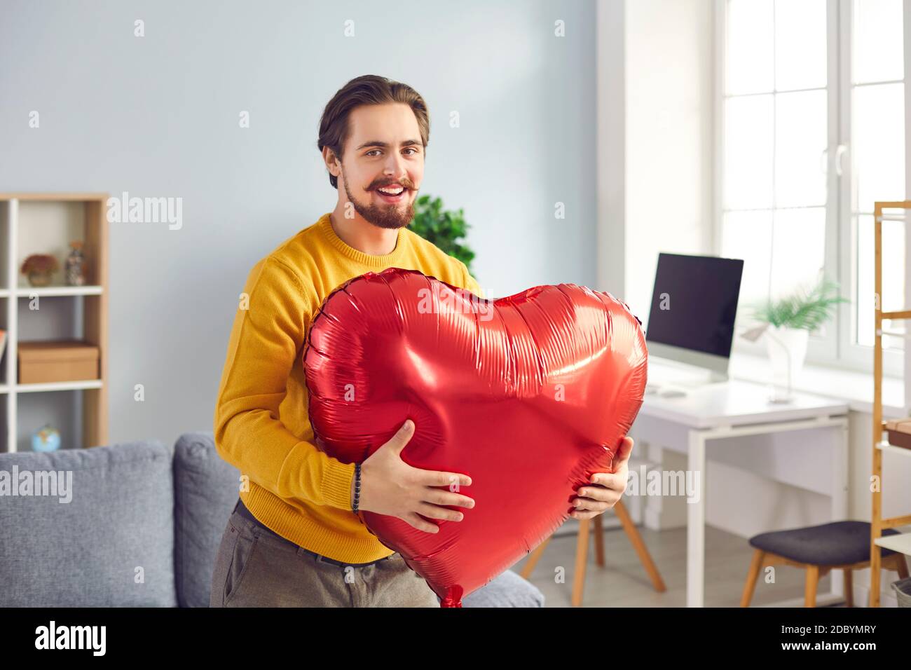 Jeune homme heureux tenant le ballon en forme de coeur qu'il a ou Donne comme cadeau romantique de Saint-Valentin Banque D'Images