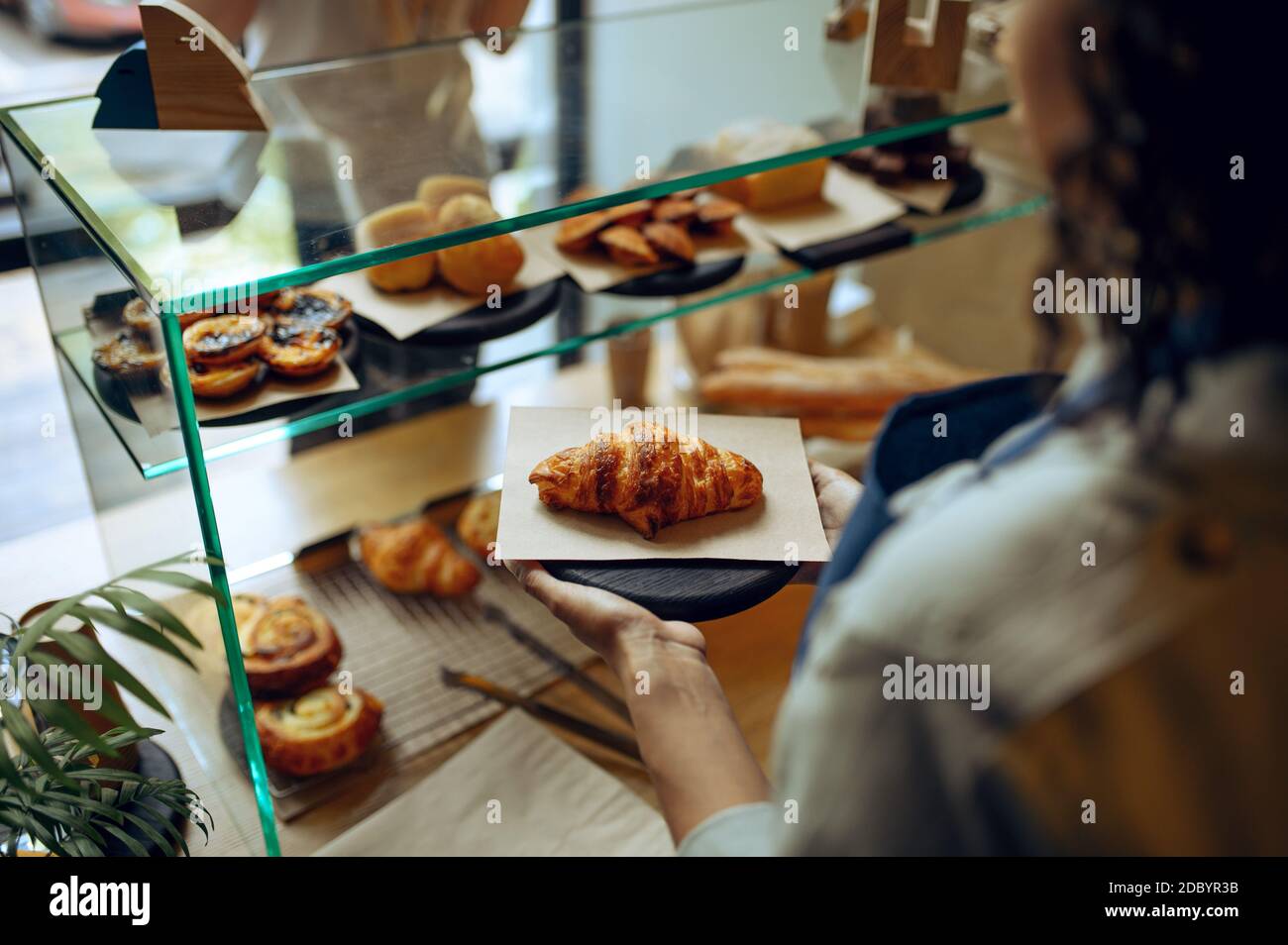 Le barista féminin en tablier prend le croissant de la vitrine au café.  Femme choisissant des bonbons à la cafétéria, serveur au comptoir au bar  Photo Stock - Alamy