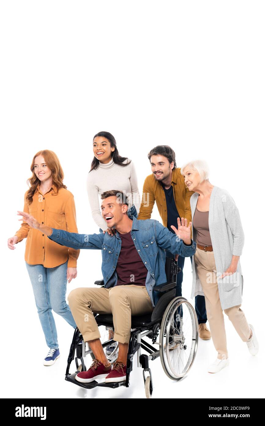 Des amis multiethniques souriants marchant près de l'homme en fauteuil roulant sur blanc arrière-plan Banque D'Images