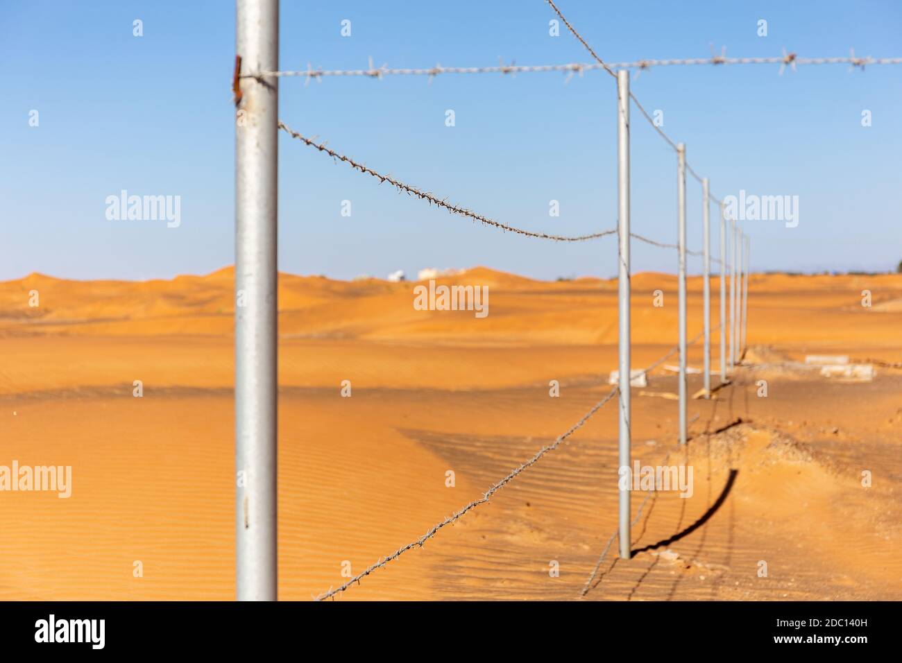 Clôture barbelée avec dunes désertiques et ciel bleu en arrière-plan dans le village fantôme d'Al Madame, Émirats arabes Unis, clôture de l'ancienne mosquée. Banque D'Images