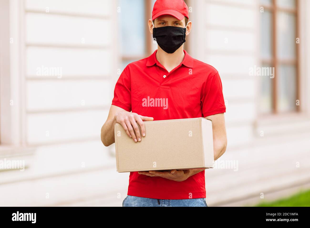 L'officier de messagerie en uniforme et masque de protection médical sur son visage tenant une boîte de carton vide, le service de livraison, Karnten, coronavirus Banque D'Images