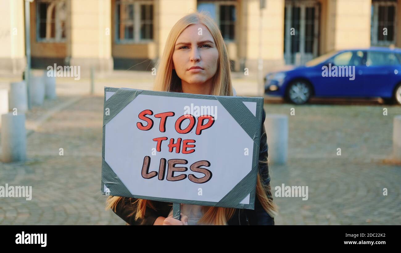 Femme préoccupée par la bannière de protestation appelant à arrêter les mensonges marche dans la rue de la ville Banque D'Images