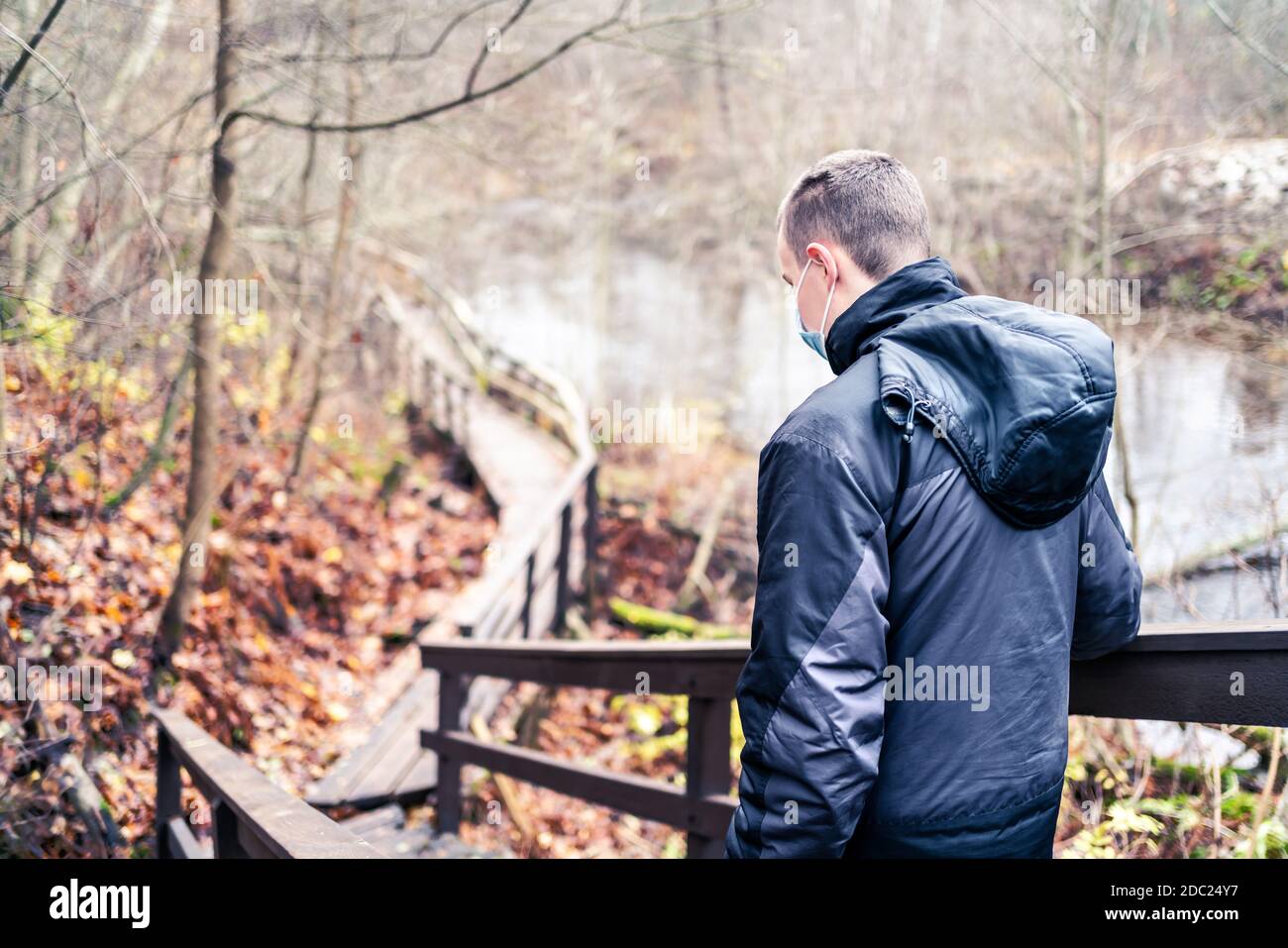 Homme portant un masque de virus corona en marchant à l'extérieur dans la nature en hiver ou en automne. Jeune personne qui fait la randonnée dans la forêt pendant une pandémie de coronavirus. Banque D'Images