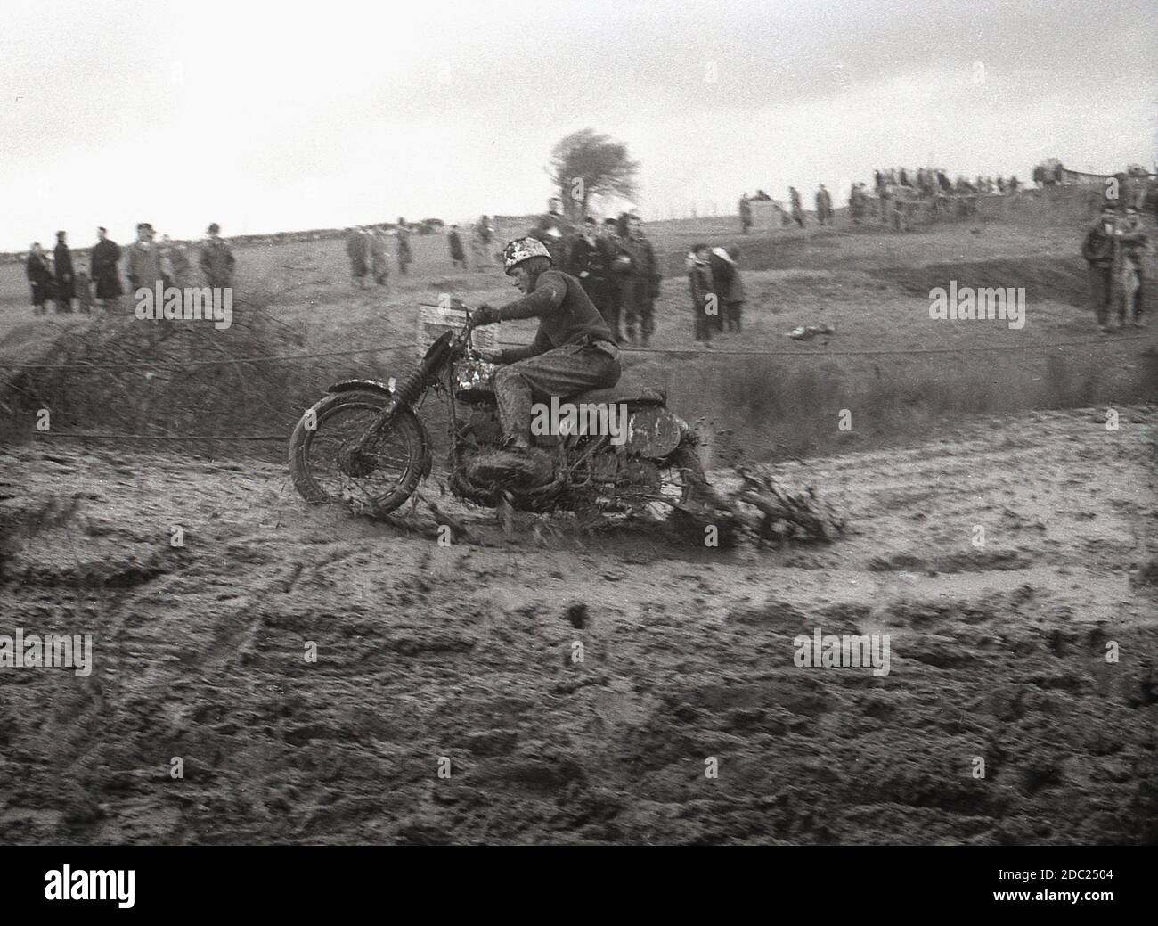 Fin des années 1950, un concurrent masculin dans un événement de brouille  de moto, en traversant un sentier boueux. Inventée en 1924, à Camberley,  Surrey, Angleterre, les motos utilisées pour se bousculer