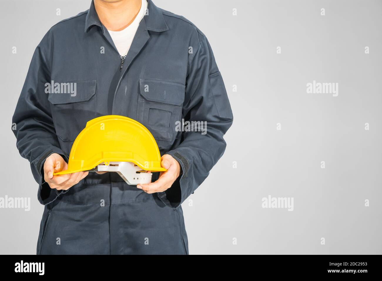 Cloes up Worker debout dans un coverall bleu tenant un casque de sécurité jaune isolé sur fond gris Banque D'Images