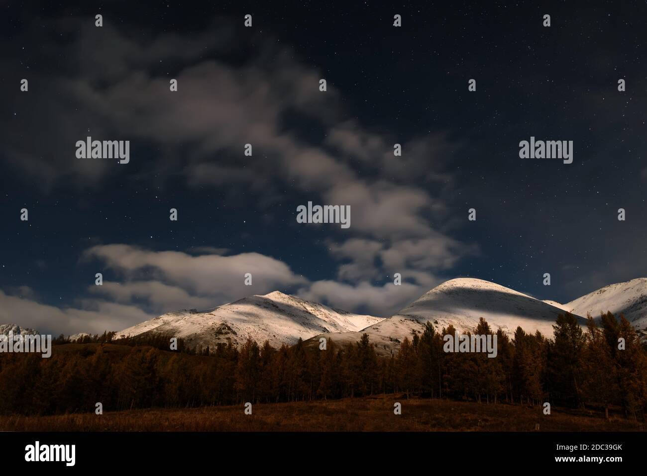 Paysage nocturne pittoresque avec nuages et étoiles dans le ciel au-dessus des montagnes enneigées et de la forêt au clair de lune en automne Banque D'Images