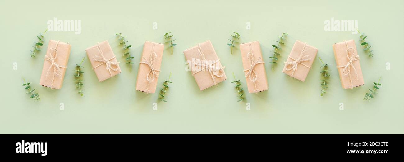 Boîtes-cadeaux en rangée enveloppées de papier kraft, nouées avec de la ficelle de jute et des brindilles naturelles d'eucalyptus sur fond vert. Holiday concept vue de dessus Flat Lay TEM Banque D'Images