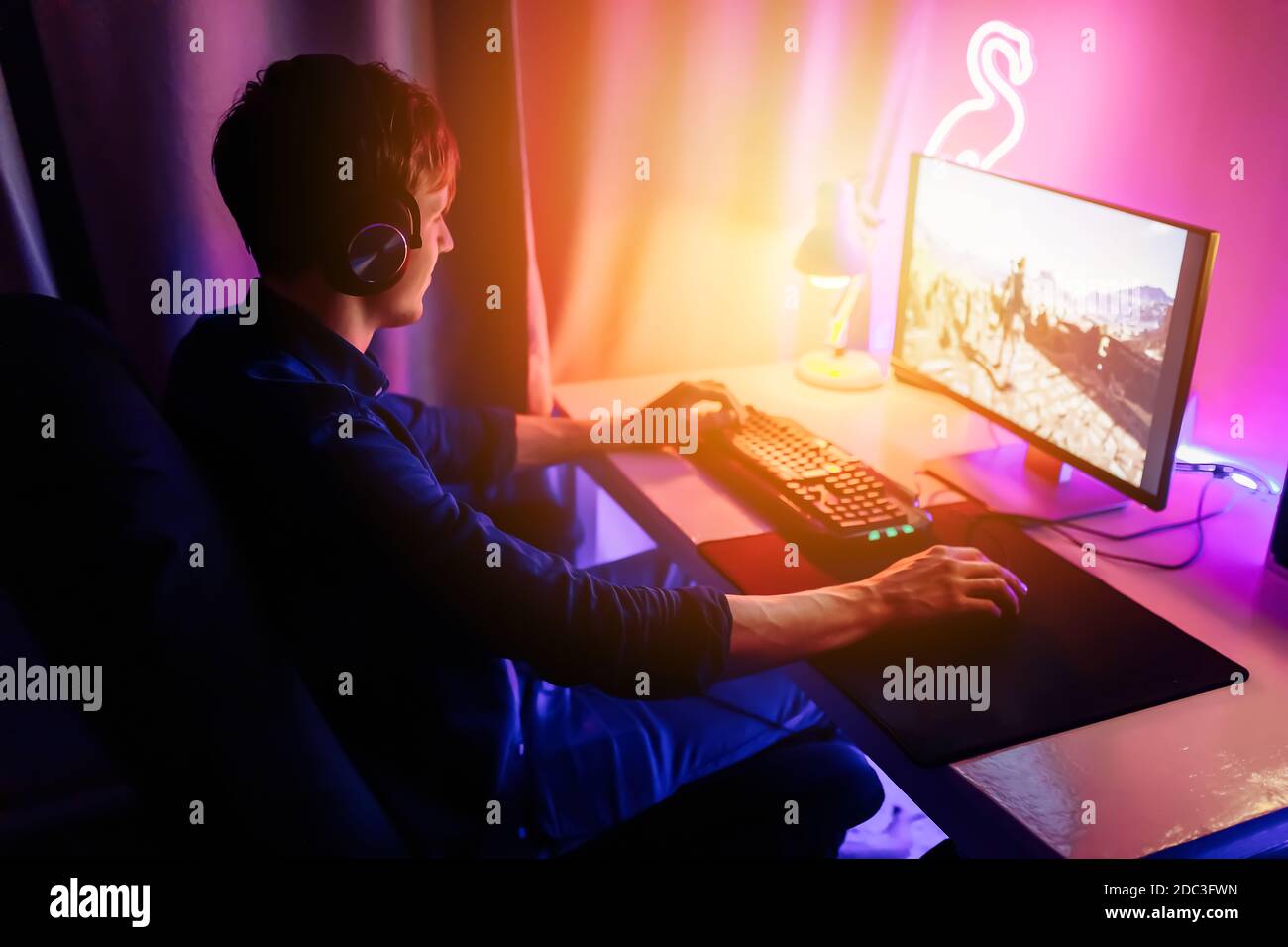 Un joueur professionnel joue à des jeux vidéo en ligne dans la première personne sur son ordinateur personnel, assis dans une pièce avec des lumières néon. Cyber sport en ligne cha Banque D'Images