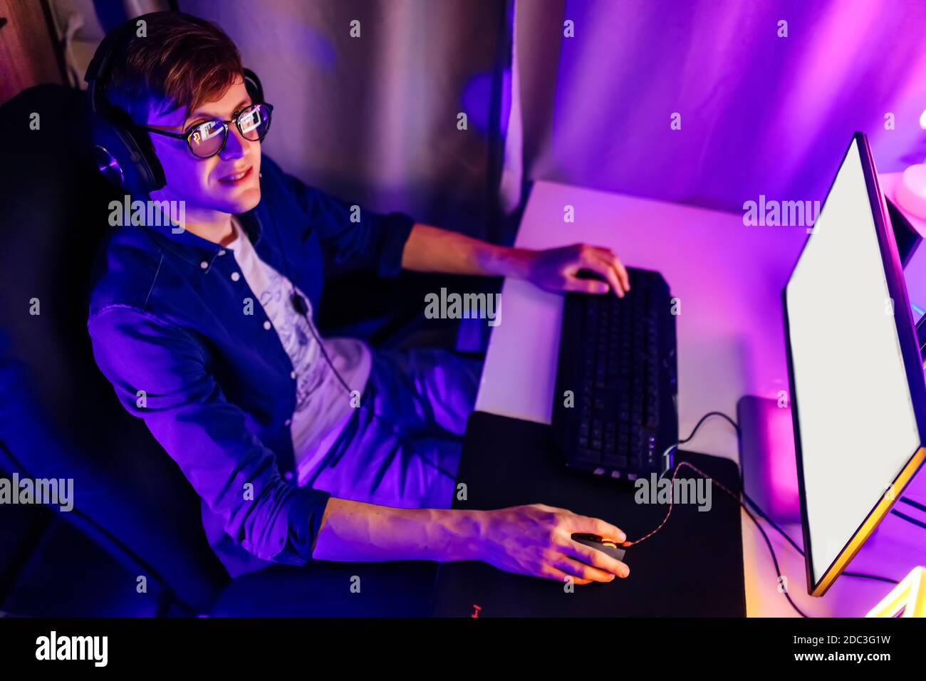 Un joueur professionnel joue à des jeux vidéo en ligne dans la première personne sur son ordinateur personnel, assis dans une pièce avec des lumières néon. Cyber sport en ligne cha Banque D'Images