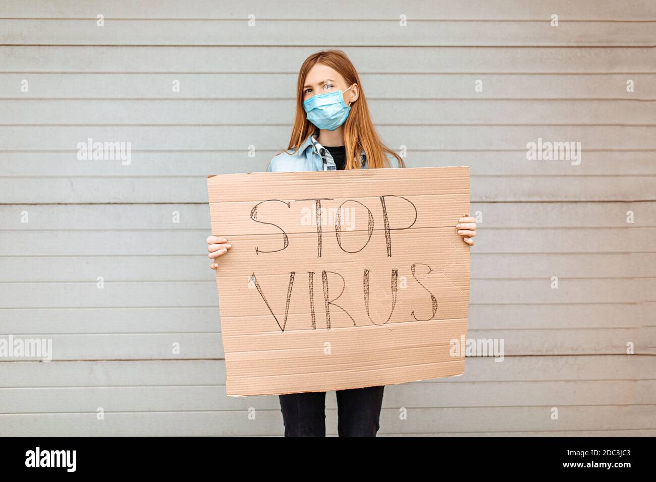 Une jeune femme dans un masque de protection médicale tient une étiquette en carton lecture Arrêtez le coronavirus, debout dans la ville contre un mur gris. Quarantin Banque D'Images