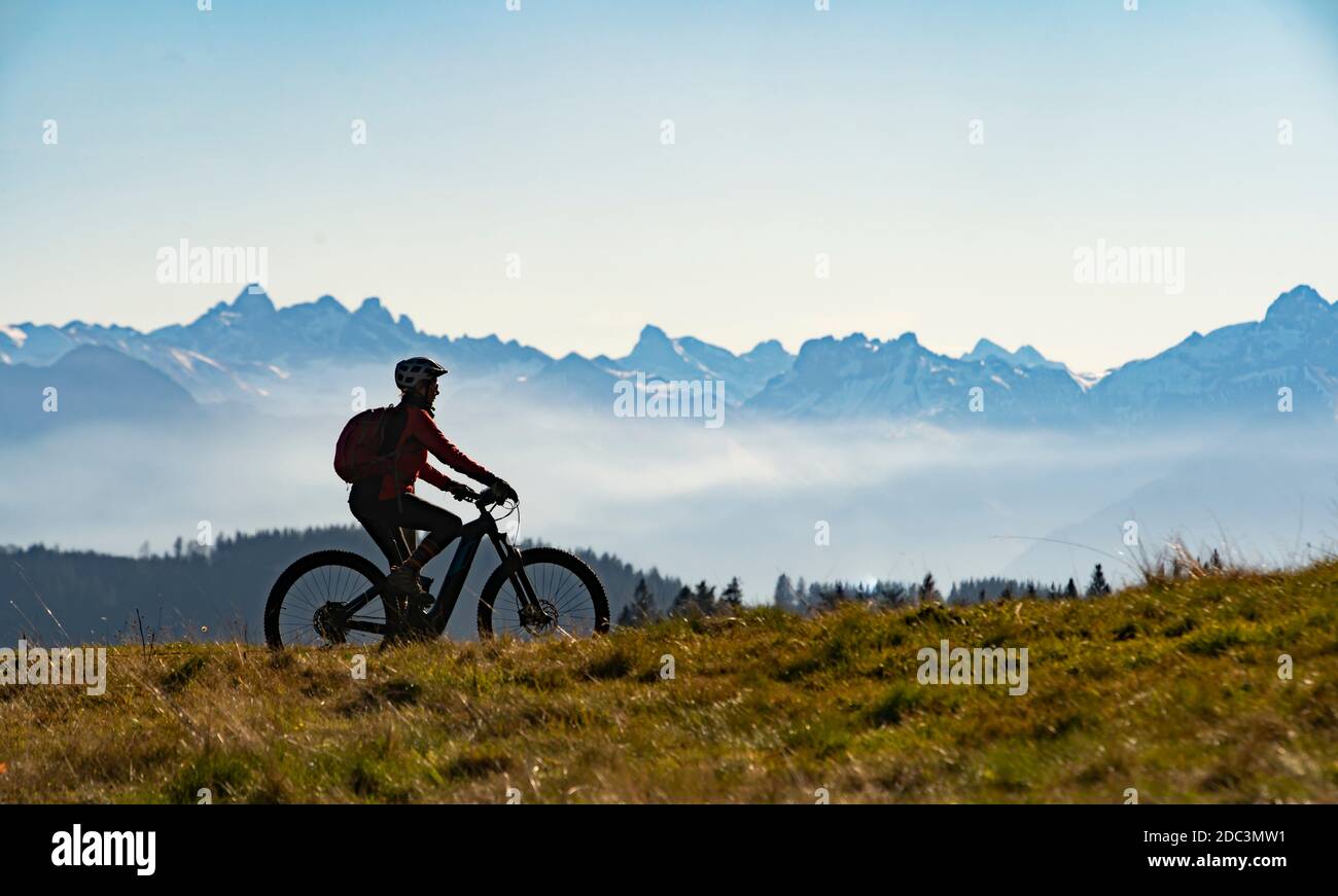 Jolie femme âgée chevauchant son VTT électrique dans les montagnes de East Allgaeu sur la chaude journée d'automne avec le mont Zugspitze en arrière-plan Banque D'Images