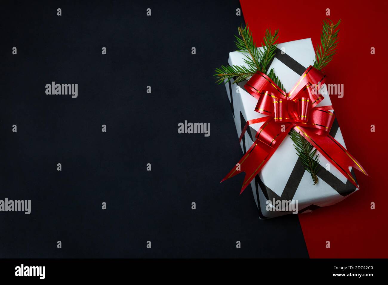 Cadeau de Noël magnifiquement emballé dans papier blanc-noir, noeud rouge, branche d'épinette, fond noir rouge. Fond de Noël, modèle pour la publicité. Banque D'Images