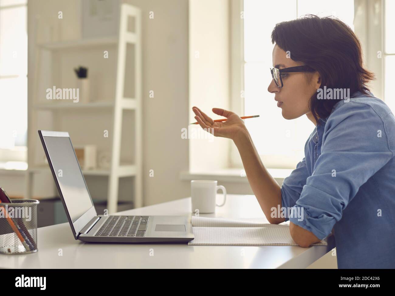 Femme assise à la maison avec un ordinateur portable et discutant de choses en ligne pendant la conversation Banque D'Images