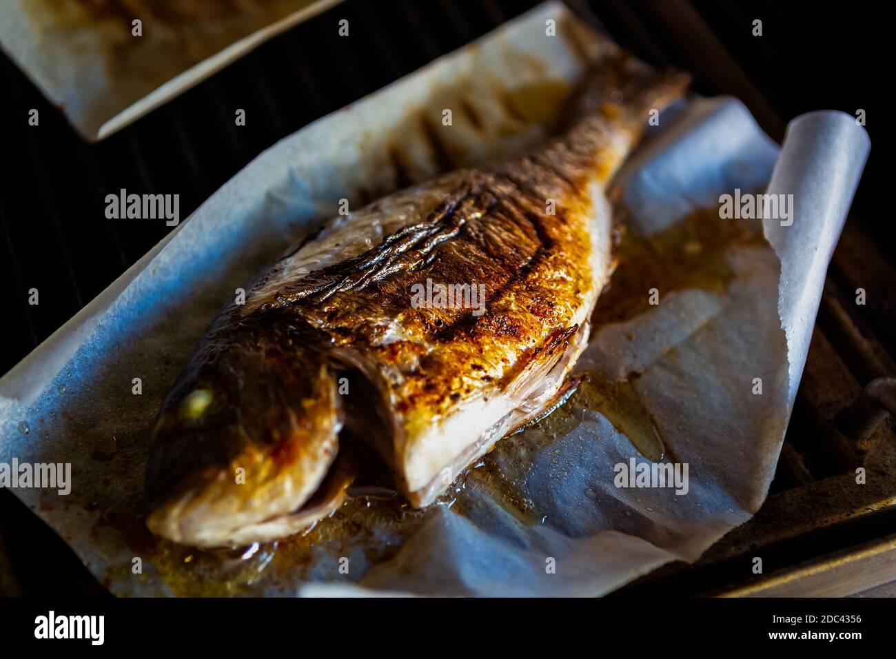 Barbecue au poisson Dorado sur papier parchemin.cuisson du bar de mer entier Faites griller en gros. Délicieux fruits de mer cuits pour le dîner Banque D'Images