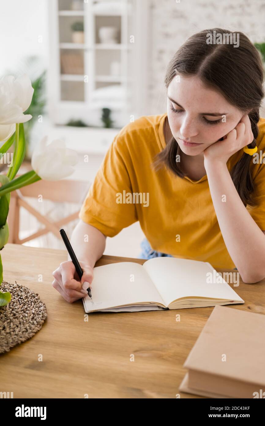 Jeune belle femme en t-shirt jaune engagé dans le travail, les affaires en ligne, étudiant assis à la table à la maison. Auto-isolement, étude, travail pendant le quaran Banque D'Images