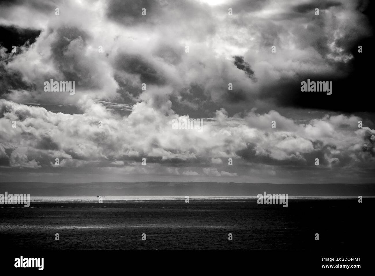 Un petit cargo descend le long du canal de Bristol sous un ciel sombre et couvant. Photographie de paysages marins en noir et blanc. Banque D'Images