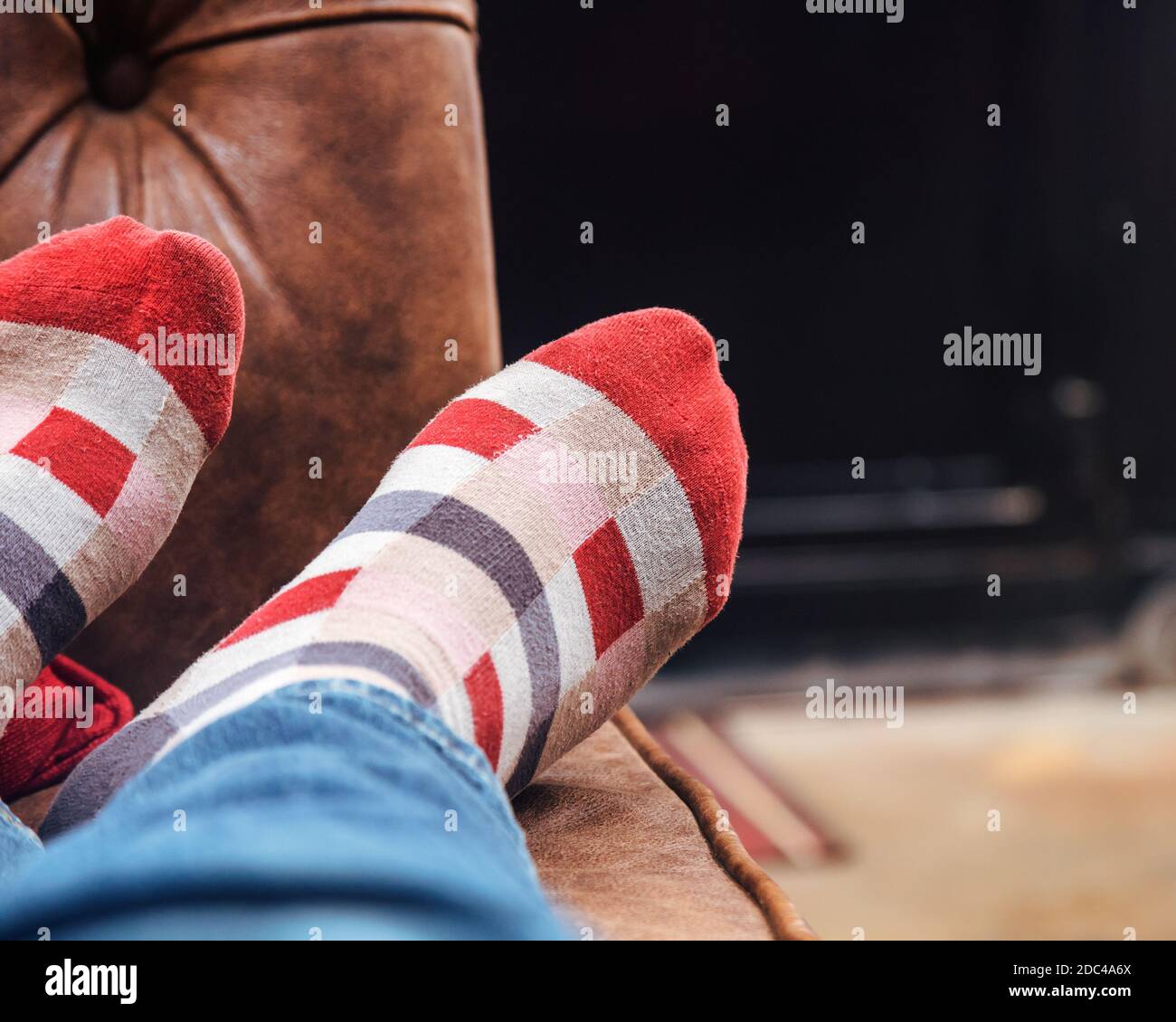 Homme avec des chaussettes à carreaux rouges prenant une sieste avec les pieds sur le canapé Banque D'Images