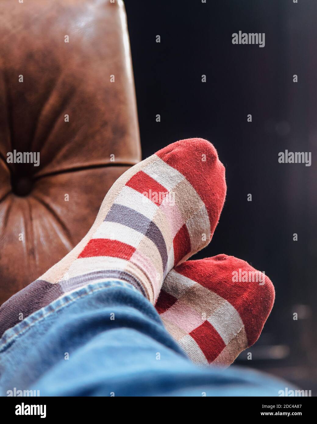 Homme avec des chaussettes à carreaux rouges prenant une sieste avec les pieds sur le canapé Banque D'Images