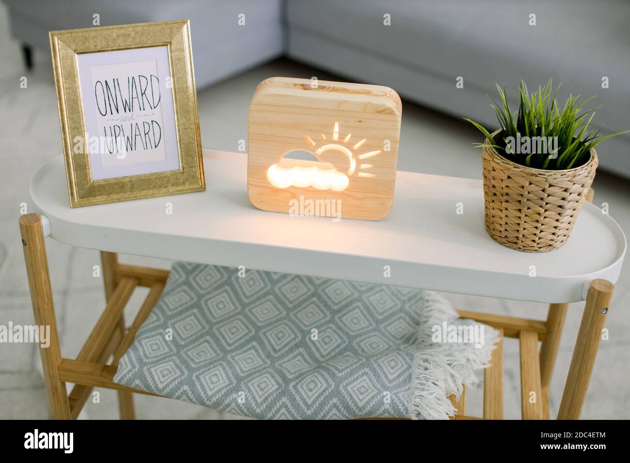 Vue en angle sur la table basse avec cadre photo, lampe décorative en bois avec soleil et image de nuage, et plante verte dans pot de fleur en osier. Fait à la main Banque D'Images
