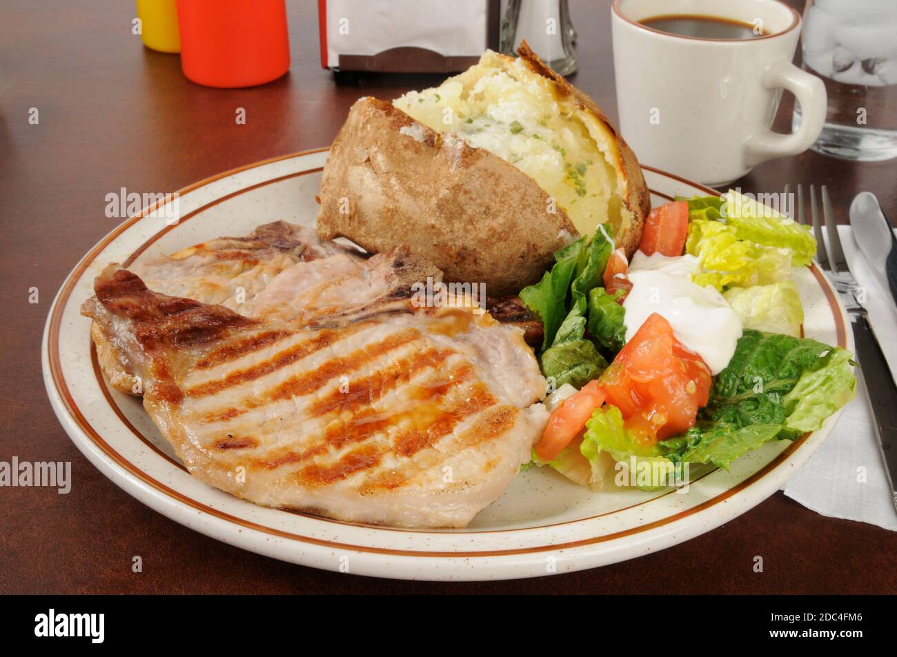 Côtelettes de porc juteuses grillées avec une pomme de terre cuite et une salade Banque D'Images