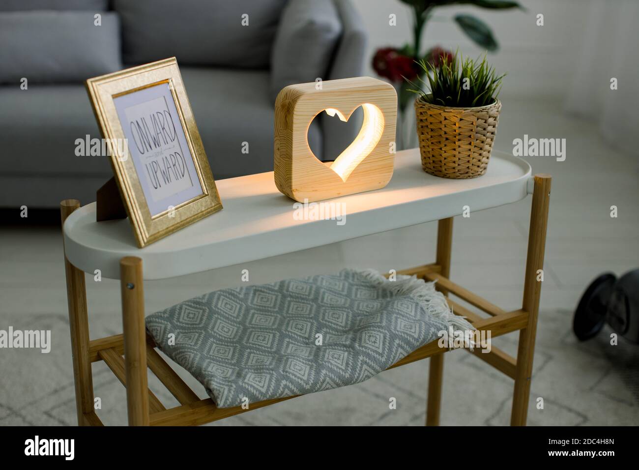 Vue en angle sur le décor fait à la main, table basse avec cadre photo, lampe décorative en bois avec photo de coeur, et plante verte dans pot de fleur en osier Banque D'Images