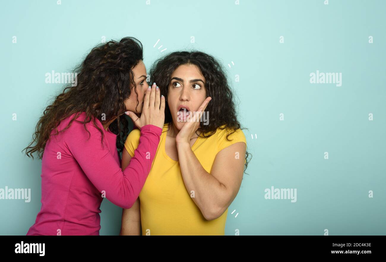 Femme parle dans l'oreille à un ami au sujet d'une grande promotion. Expression stupéfait. Fond cyan Banque D'Images