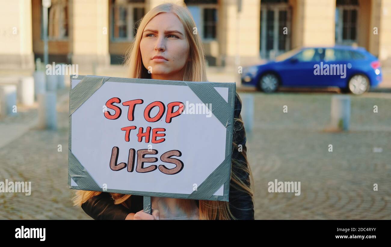 Femme préoccupée par la bannière de protestation appelant à arrêter les mensonges marche dans la rue de la ville Banque D'Images
