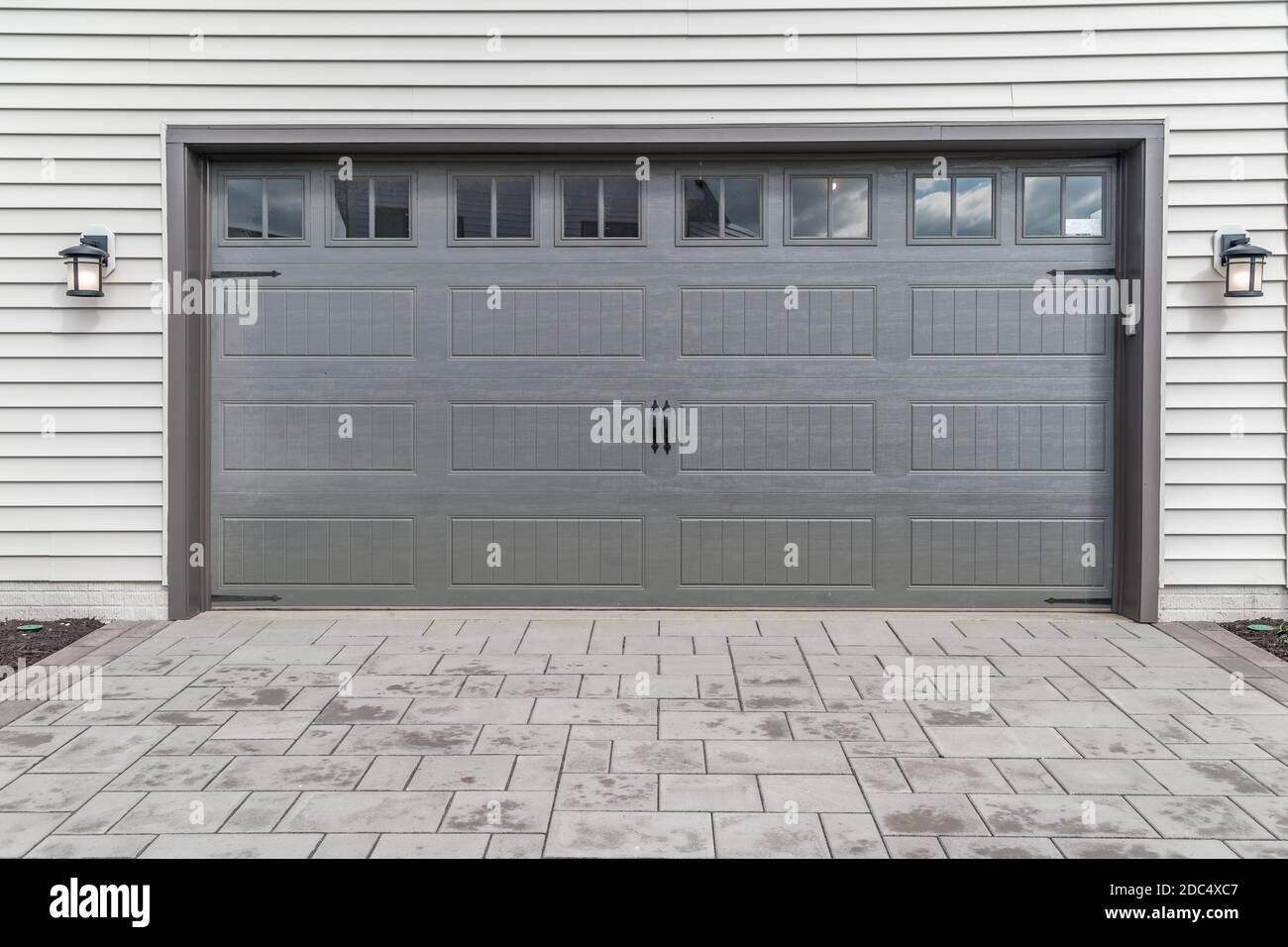 Porte de garage grise à deux voitures avec cadre en pierre architecturale pour ajouter de l'accent, avec fenêtres claires en tableau divisé par des barbecues pour muntins Banque D'Images