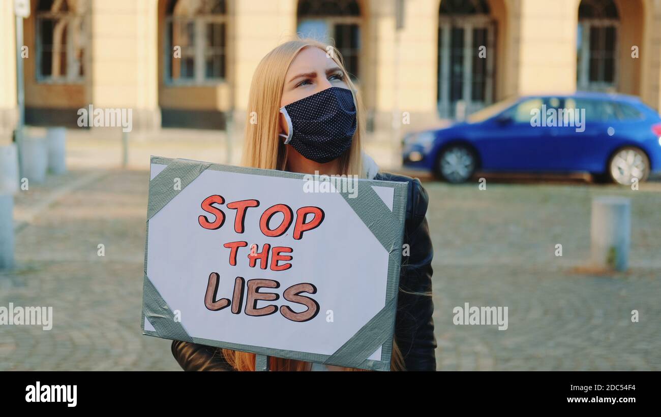 Femme inquiète dans un masque de protection avec une bannière de protestation appelant à arrêtez-vous en marchant dans la rue de la ville Banque D'Images