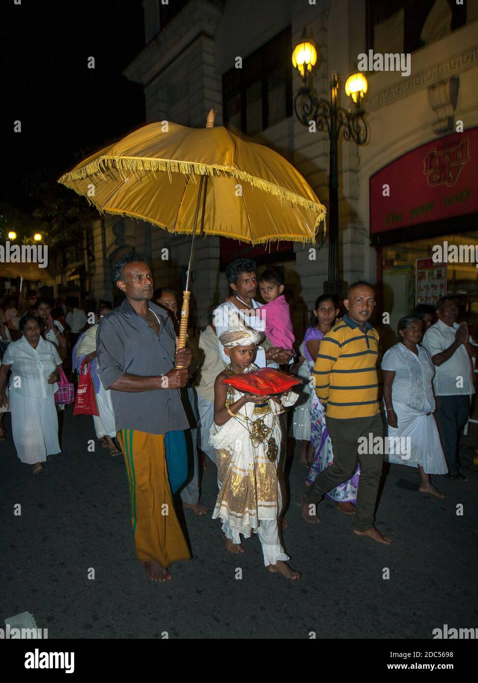 Un garçon est abrité par un parapluie lors d'une petite perahera bouddhiste (procession) qui a lieu à 4 heures du matin dans une rue à Kandy, Sri Lanka. Banque D'Images