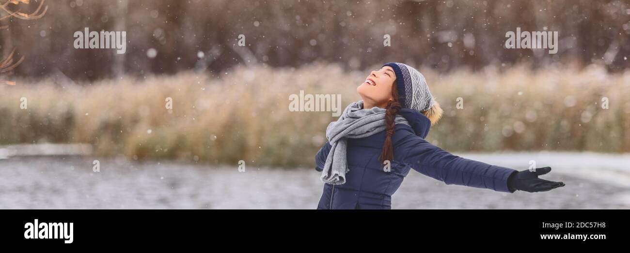 Neige hiver bonne fille asiatique avec les bras ouverts appréciant la neige chute flocons de neige porter foulard temps froid, chapeau, gants chaud veste bannière Banque D'Images