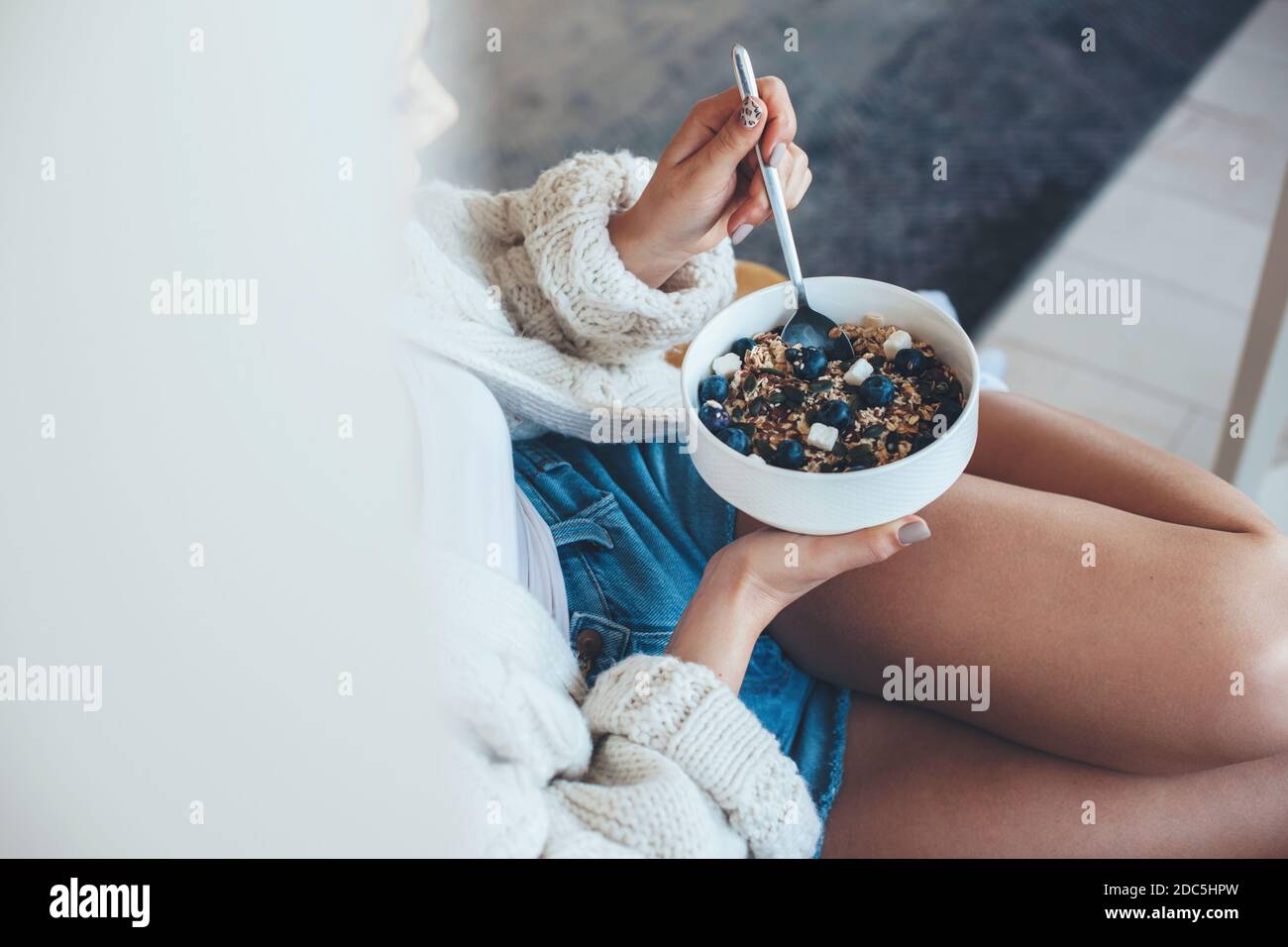 Photo d'une femme mangeant des céréales avec des fruits et mentant sur quelque chose dans un pull Banque D'Images