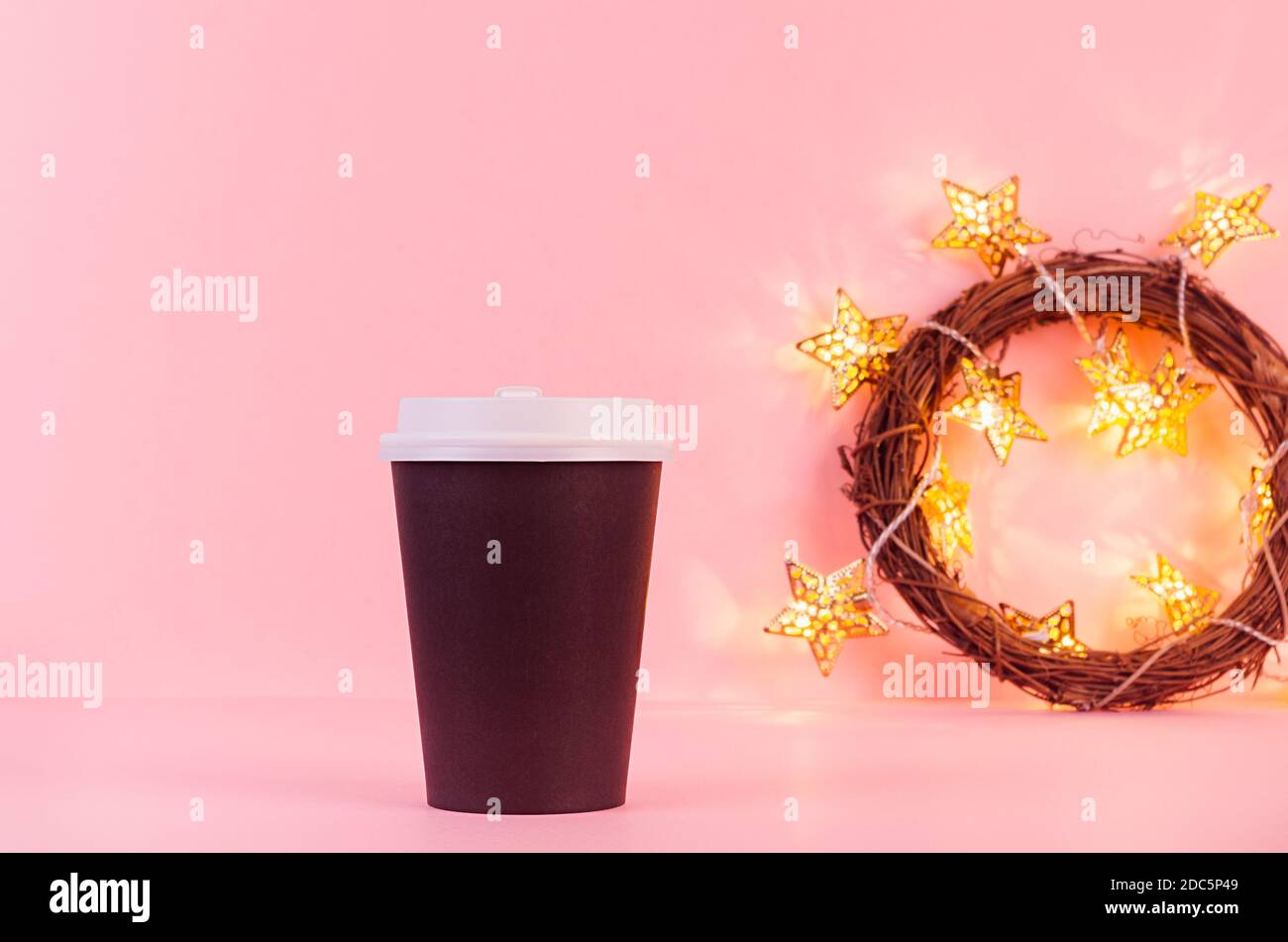 Maquette de grande tasse en papier de café noir avec lumières de noël dorées sur fond rose, modèle pour la publicité, le design, le café, le restaurant, le bar. Banque D'Images Maquette de grande tasse en papier de café noir avec lumières de noël dorées sur fond rose, modèle pour la publicité, le design, le café, le restaurant, le bar. Banque D'Images