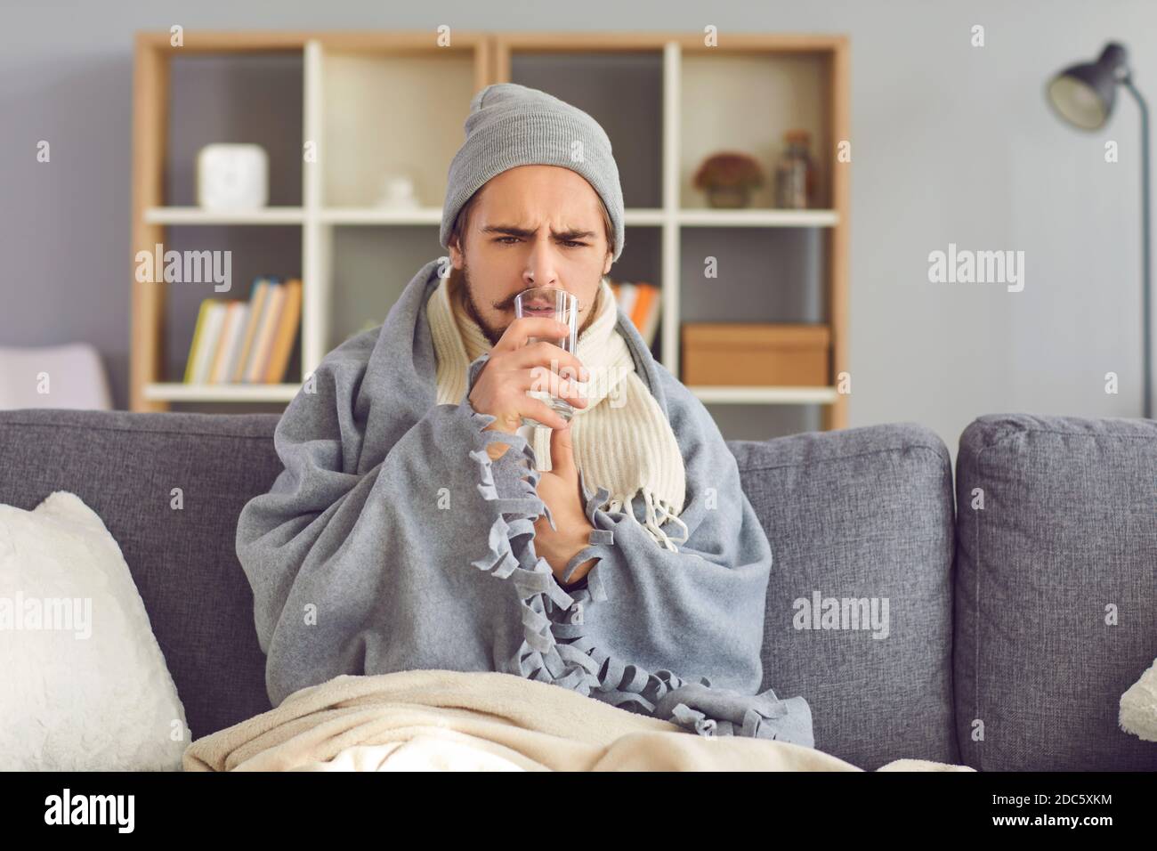Malheureux malade homme assis sur un canapé enveloppé dans une couverture et prendre des médicaments avec de l'eau Banque D'Images