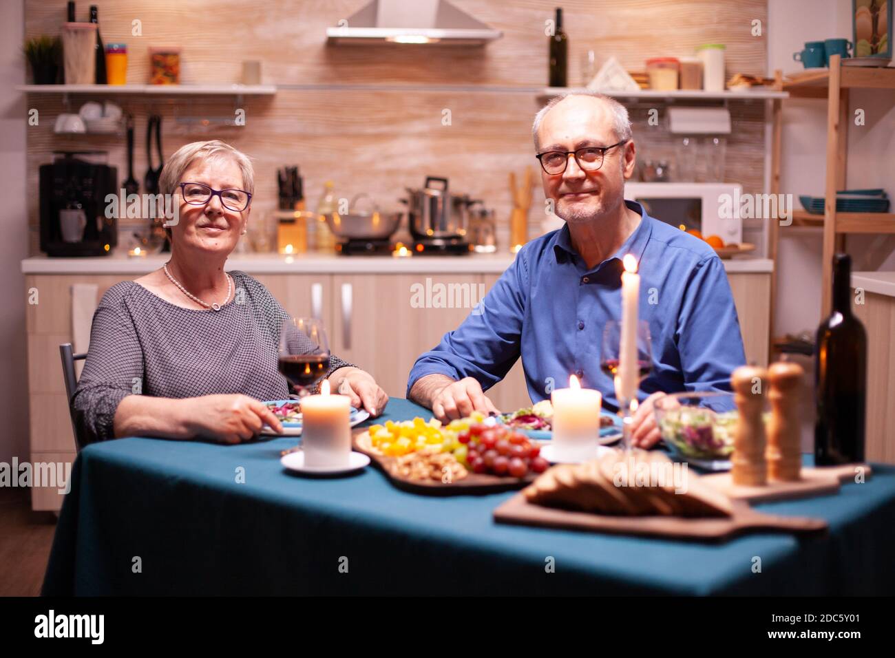Couple senior regardant l'appareil photo pendant la célébration de la relation avec un dîner de fête dans la cuisine. Anniversaire, loisirs, retraite, famille, romantique Banque D'Images