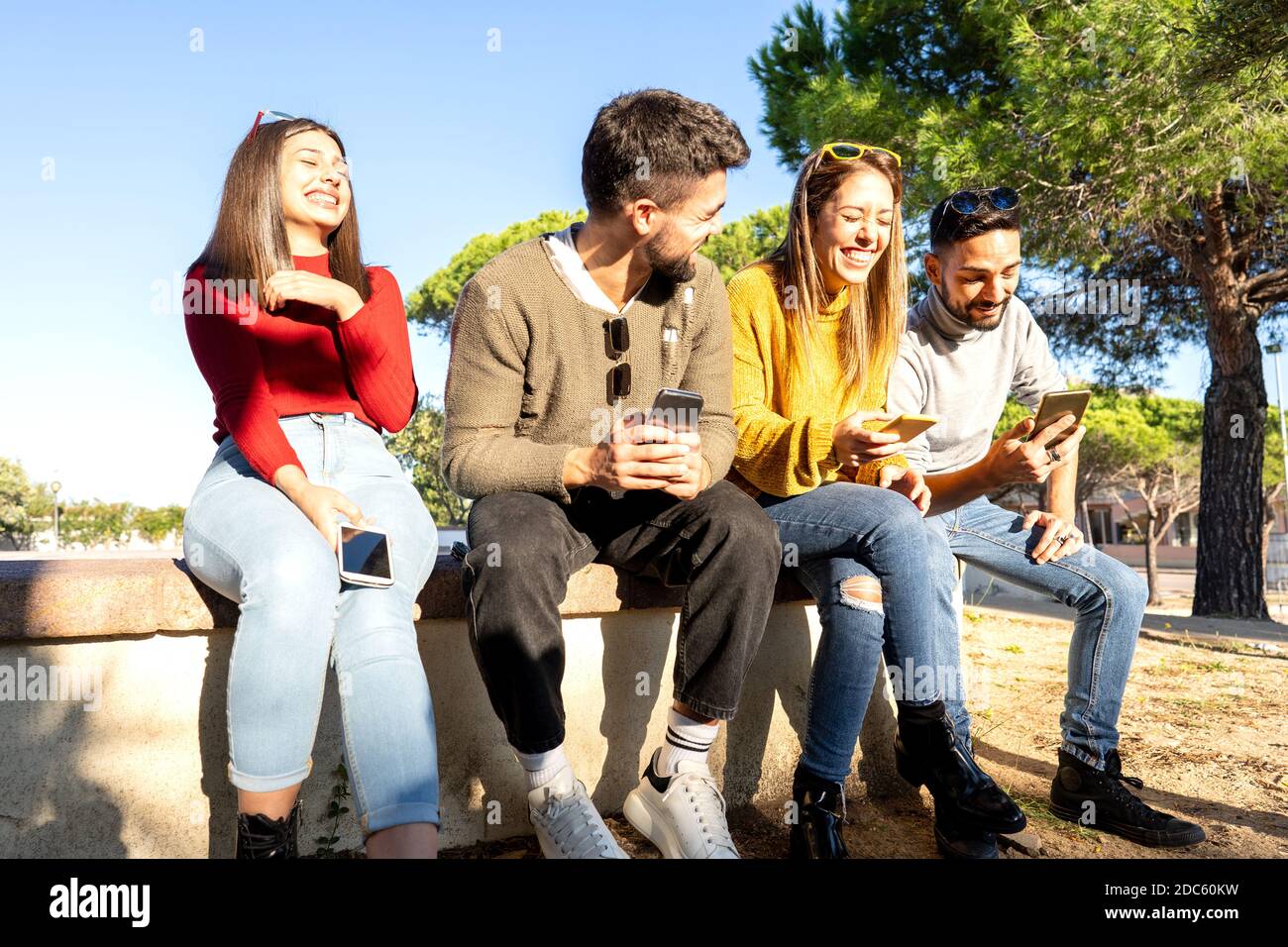 Deux jeunes couples hétérosexuels en train de rire les uns les autres à l'aide d'un smartphone Pour discuter en ligne - heureux millénaire groupe de personnes ayant plein air amusant Banque D'Images