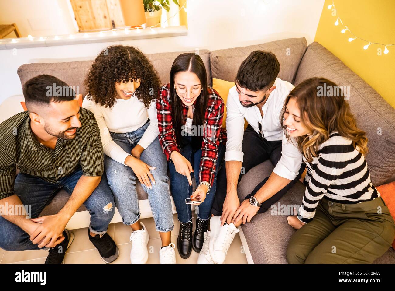 Groupe d'amis de course mixte s'amusant à la maison assis Sur le canapé regardant le smartphone - multiracial jeune personnes utilisant le réseau social pour partager Banque D'Images