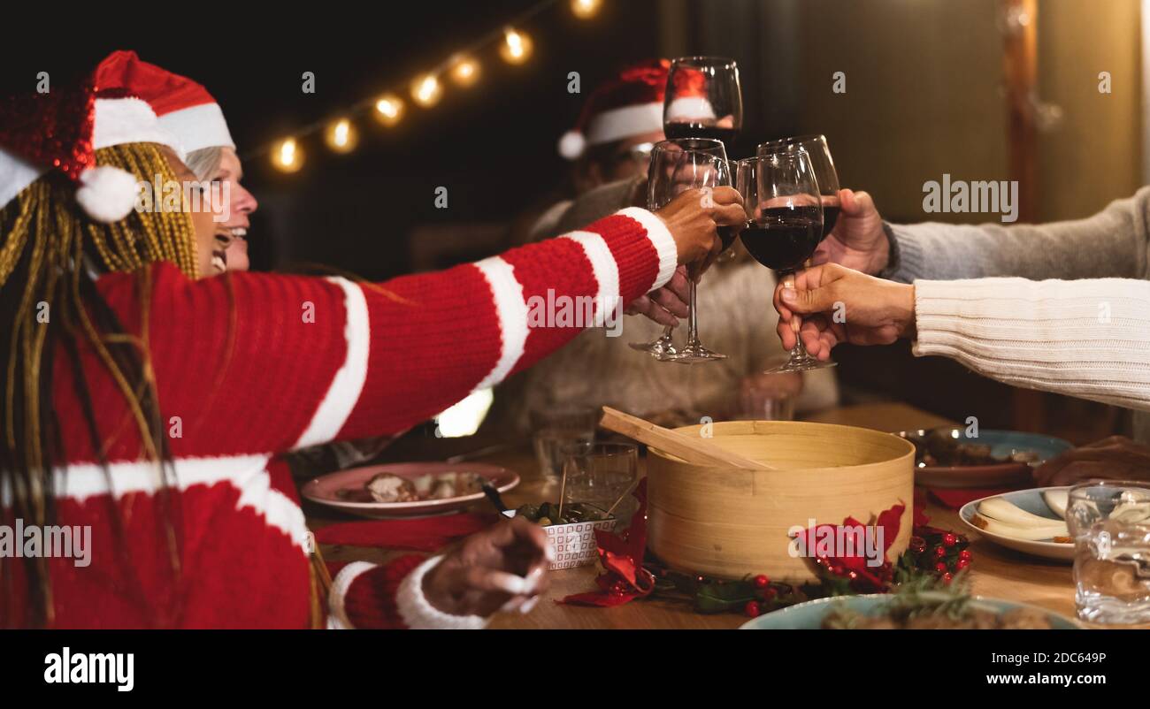 De joyeux amis multiraciaux âgés de griller avec des verres à vin rouge pendant Fêtes de Noël dîner sur le patio maison fête Banque D'Images