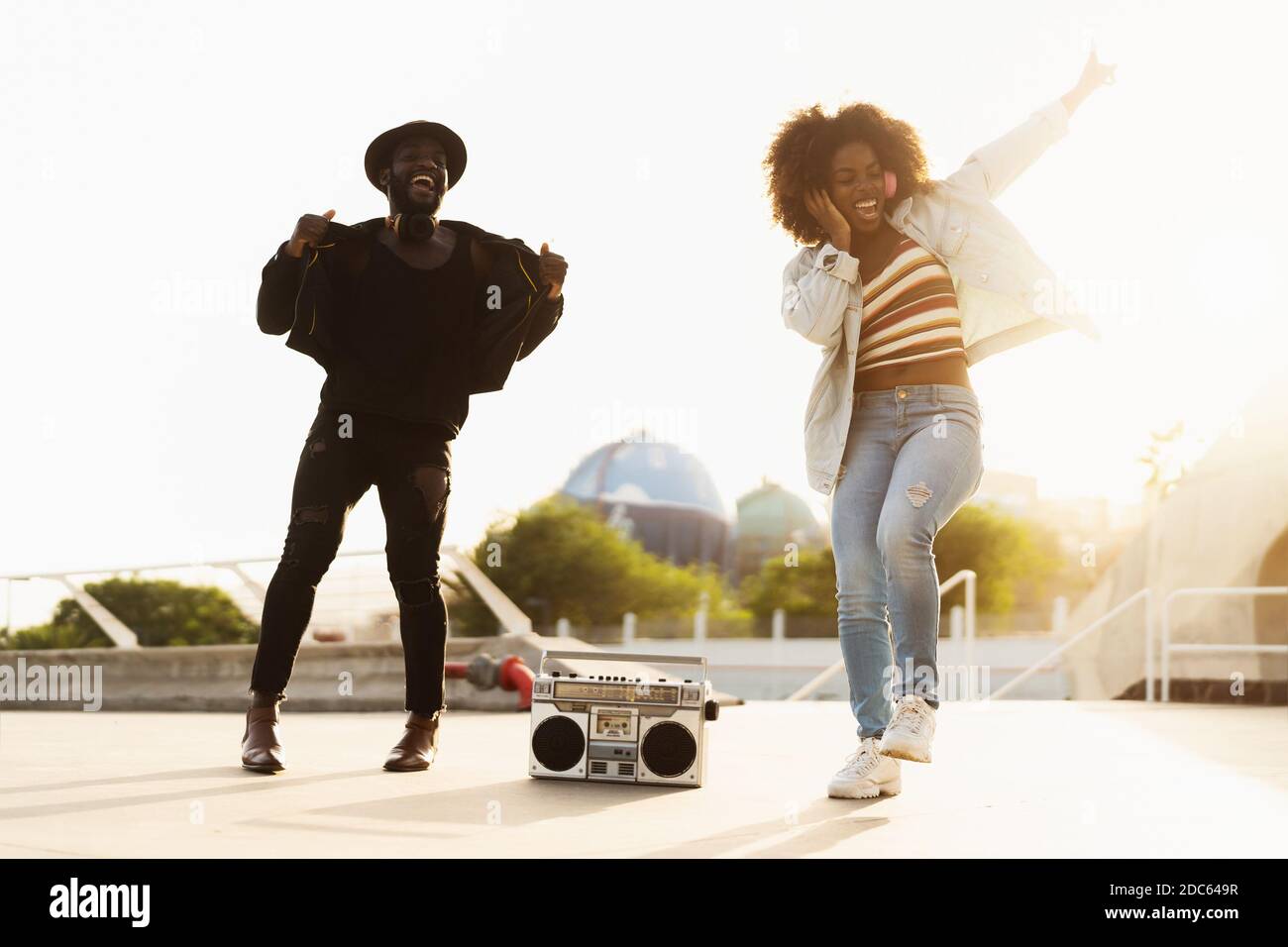 De jeunes amis afro dansent en plein air tout en écoutant de la musique avec casque sans fil et boombox vintage Banque D'Images