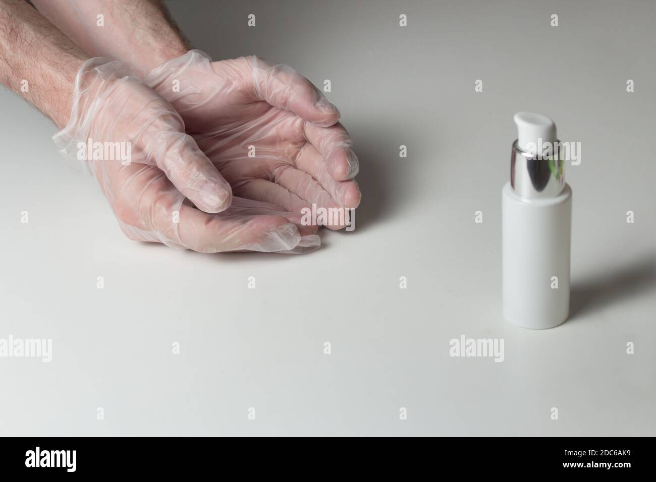 Deux mains en gants blancs semi-transparents et une bouteille de gel hydroalcoolique sur une table blanche. Équipement de protection Covid-19. Banque D'Images