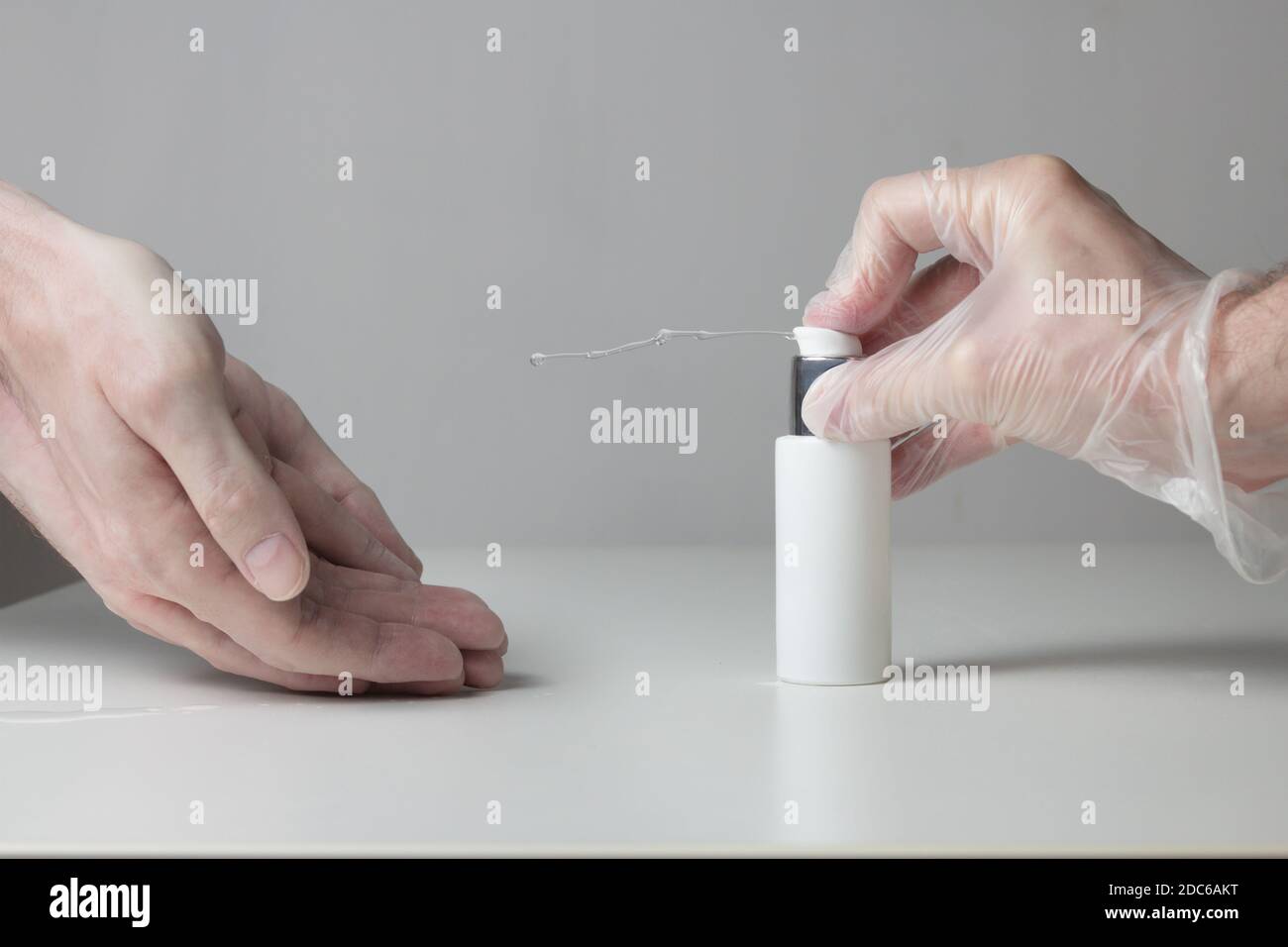 Un jet de gel désinfectant hydroalcoolique sort du flacon appuyé par une main gantée tandis que les mains sales attendent de recevoir le liquide. Banque D'Images