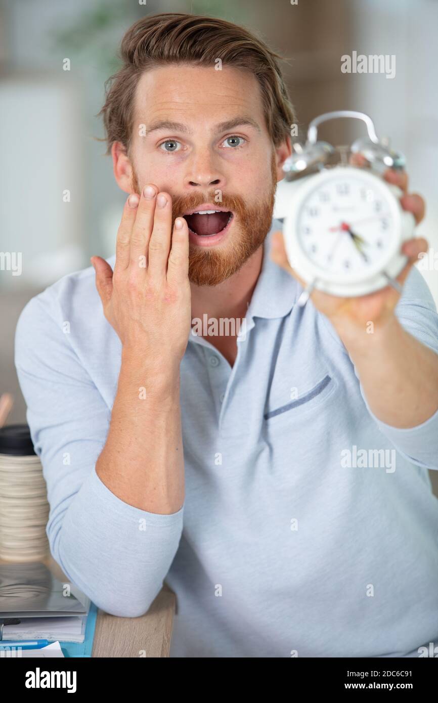 un jeune homme d'affaires choqué tient une horloge à son bureau Banque D'Images