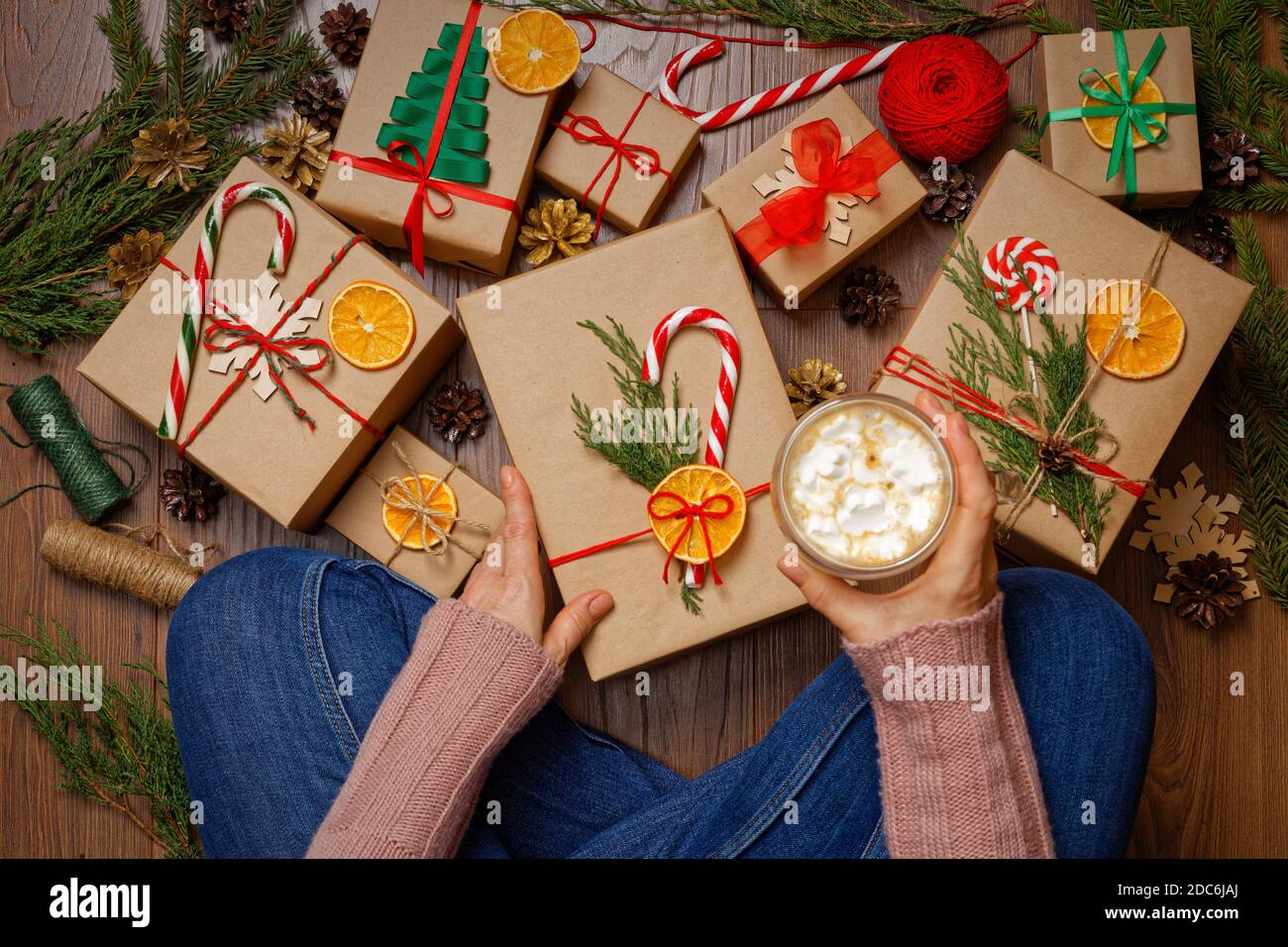 Une fille assise sur le sol devant un bouquet de boîtes cadeaux de noël et tient dans la main une tasse de cappuccino avec guimauve. Vue de dessus. Banque D'Images Une fille assise sur le sol devant un bouquet de boîtes cadeaux de noël et tient dans la main une tasse de cappuccino avec guimauve. Vue de dessus. Banque D'Images