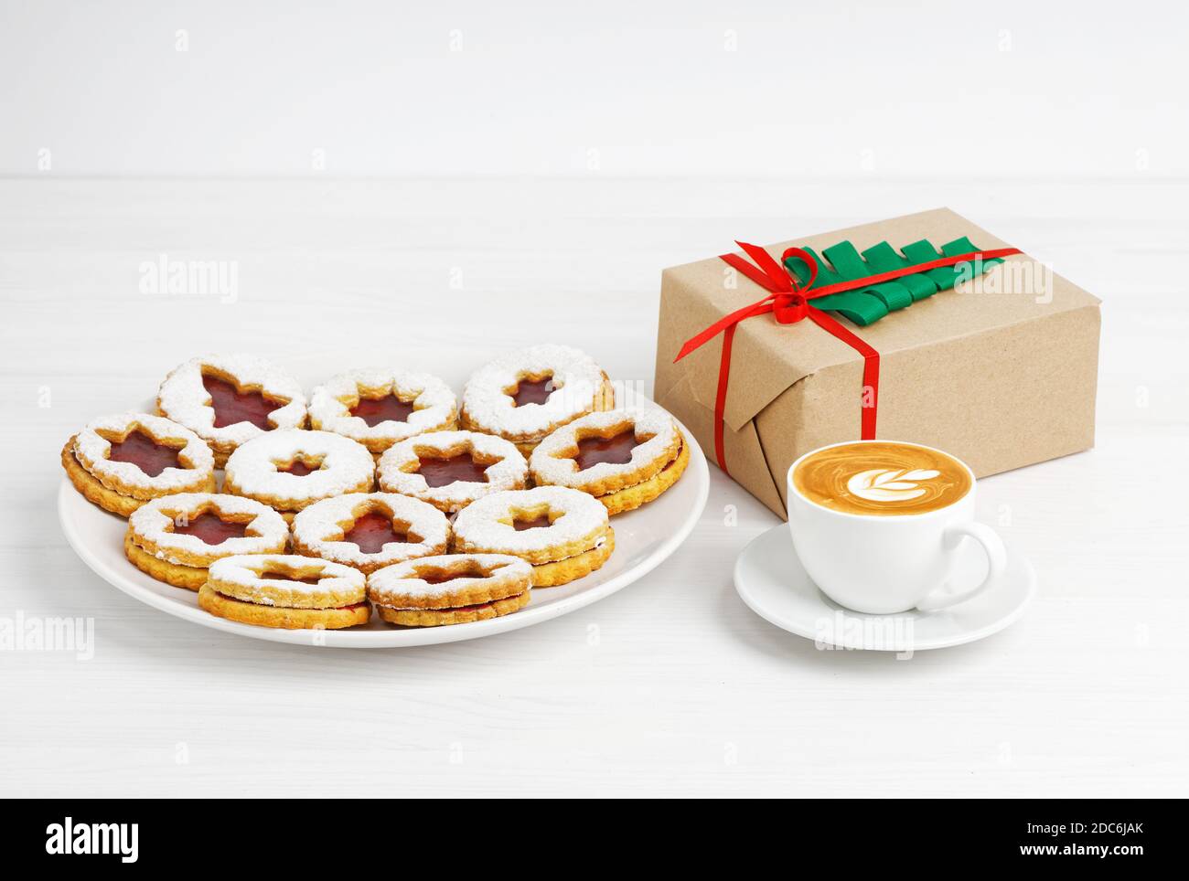 Tasse de café, biscuits faits maison et boîte cadeau enveloppée de papier kraft décoré d'un ruban vert en forme d'arbre de Noël sur une patte en bois blanc Banque D'Images Tasse de café, biscuits faits maison et boîte cadeau enveloppée de papier kraft décoré d'un ruban vert en forme d'arbre de Noël sur une patte en bois blanc Banque D'Images