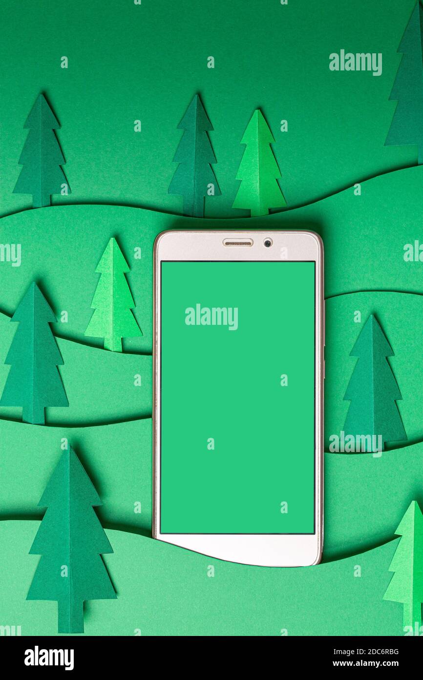Maquette 3D en papier arbres de Noël avec Smart phone sur fond vert. Carte de Noël à motif de découpe de papier avec espace de copie. Haut v Banque D'Images