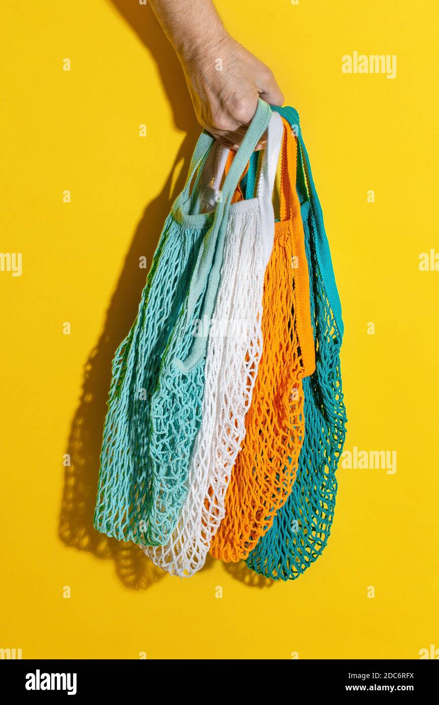 Main d'homme tenant des sacs vides en filet sur fond jaune. Sac écologique sans déchets. Achats gratuits en plastique. Substance écologique pour la maison. Sac de ficelle pour Banque D'Images