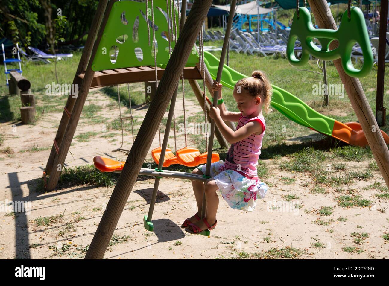 Petite fille blonde jouant dans le parc, balançant Banque D'Images