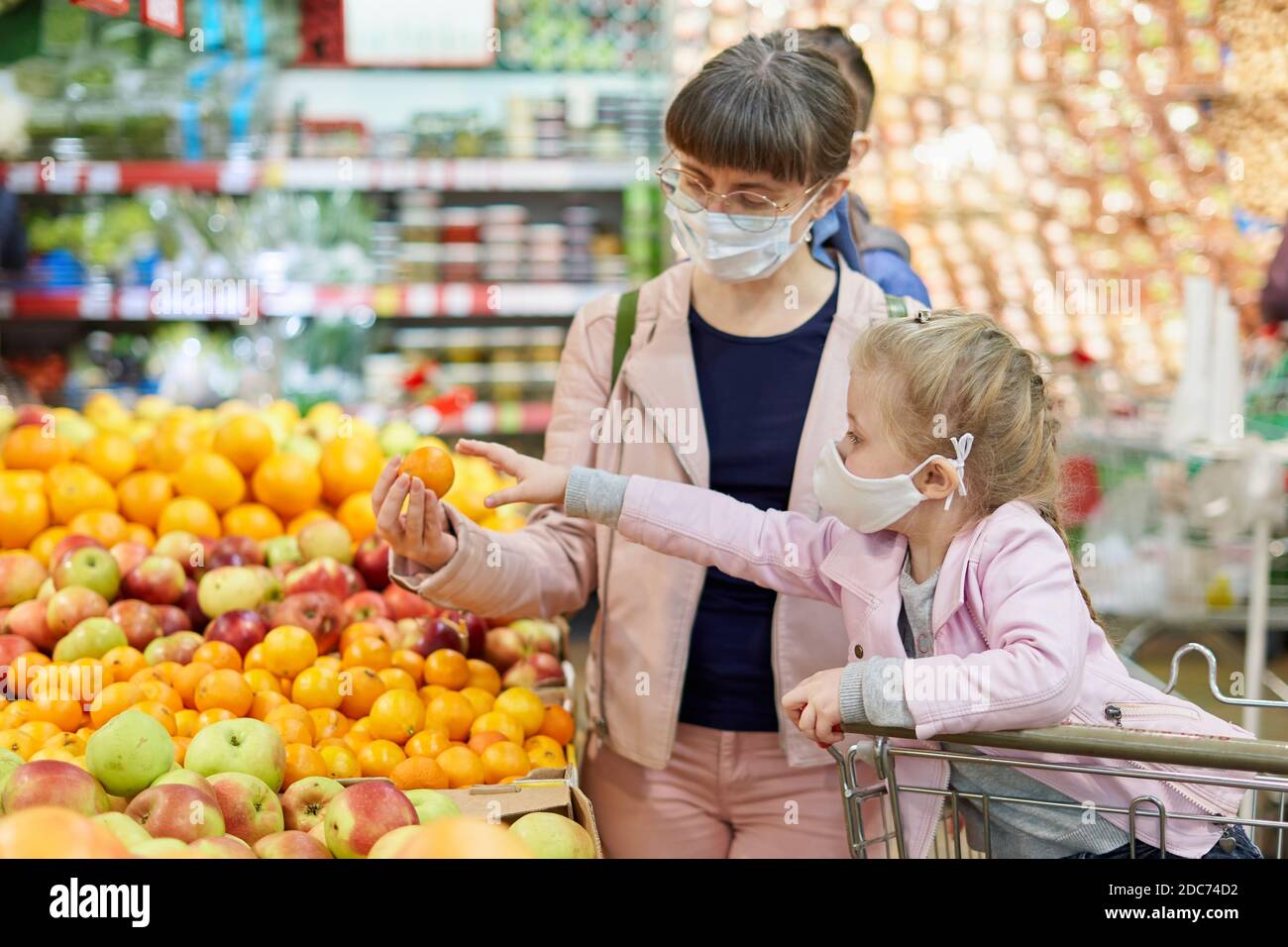 Maman et fille portant des masques protecteurs choisissent des fruits à acheter dans le magasin Banque D'Images