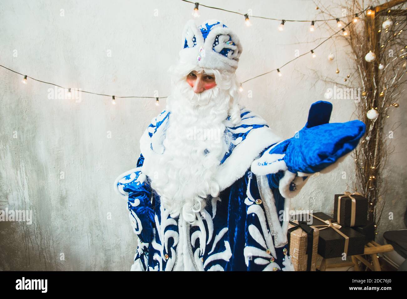 Le Père Noël en fourrure bleue se dresse sur le fond d'une guirlande du nouvel an et pointe avec sa main gantée vers la caméra. Banque D'Images