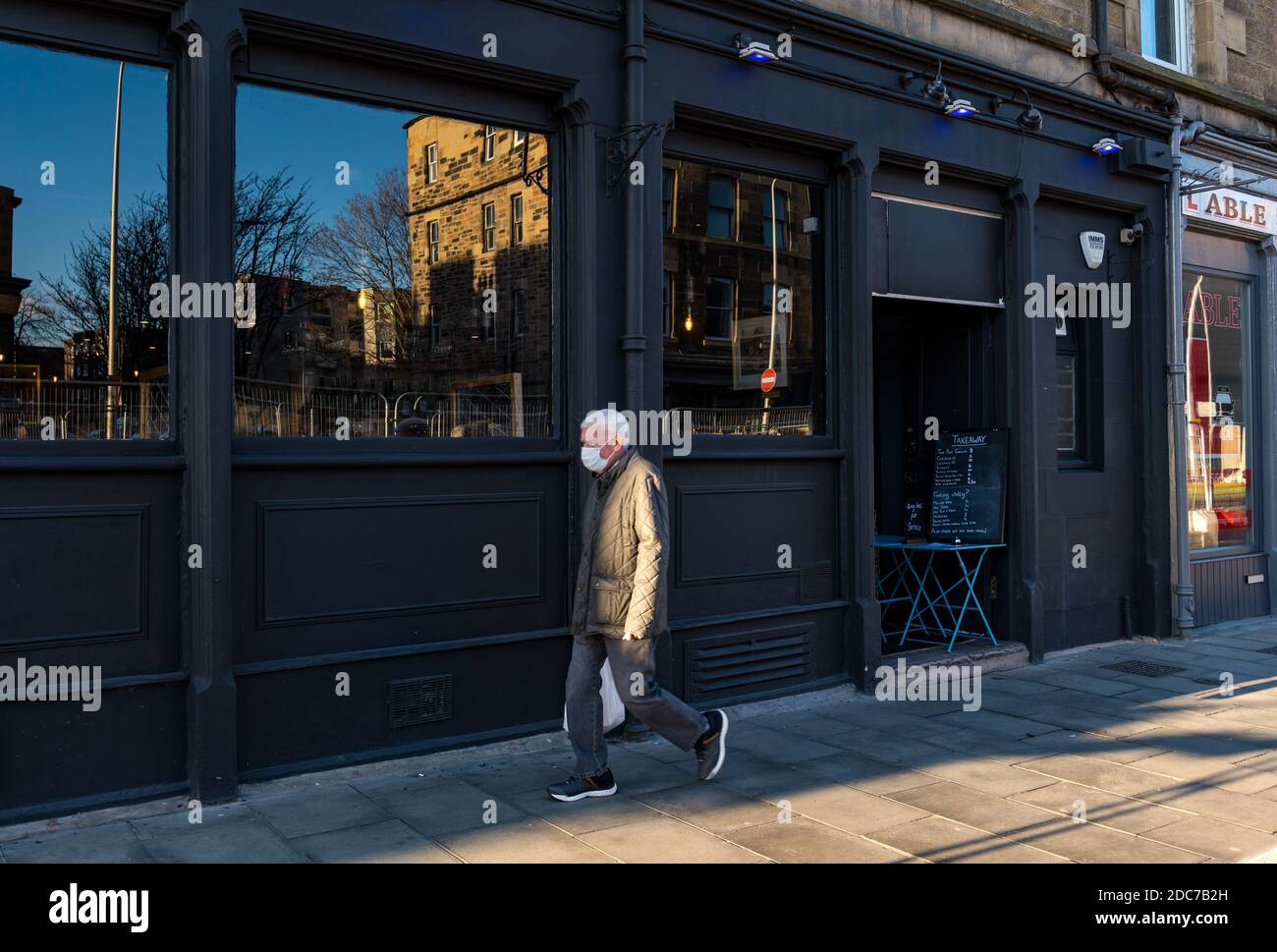 Leith, Édimbourg, Écosse, Royaume-Uni, 19 novembre 2020. Covid-19 Life: Certains pubs sont fermés tandis que d'autres servent de la bière à emporter et des boissons. La mère supérieure de Leith Walk sert des boissons à emporter avec une cloche sur la table pour convoquer un membre du personnel comme un homme portant un masque de visage qui passe devant Banque D'Images